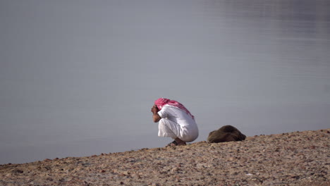 Egyptian-Man-in-Traditional-Clothes-With-Turban-Washing-Face-on-Riverbank,-Wide-View