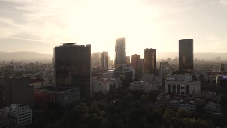 Filmische-Luftaufnahme-Der-Skyline-Der-Innenstadt-Von-Mexiko-Stadt-Mit-Hintergrundbeleuchtung-Bei-Sonnenuntergang