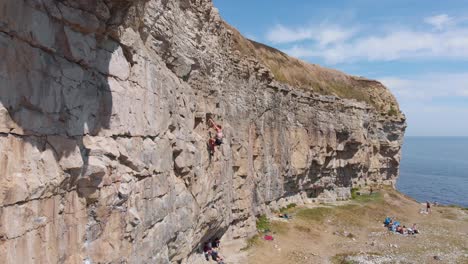 Aerial-Dolly-of-Strong-Girl-Rock-Climbing-At-Sunny-British-Coastline