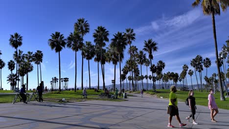 People-walking-past-camera-at-Venice-Beach-Boardwalk-with-police-in-the-background-in-Los-Angeles,-California,-USA