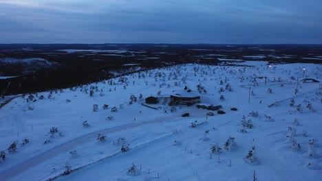 Aerial-view-of-a-car-leaving-the-Tuikku-restaurant-on-top-of-the-Levi-mountain,-polar-night-in-Lapland---reverse,-drone-shot