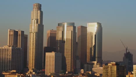 Aerial-view-of-sunlit-skyscrapers-in-Downtown,-Los-Angeles,-California,-USA,-during-sunset---Descending-and-panning,-drone-shot