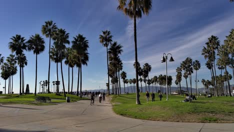 People-walking-and-riding-bikes-at-the-Venice-Beach-Boardwalk-on-a-nice-sunny-afternoon-in-Los-Angeles,-California,-USA---Wide-shot