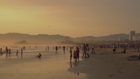 Santa-Monica-Beach,-Malerische-Sonnenuntergangslandschaft,-Silhouetten-Von-Menschen,-Pier-Und-Riesenrad-Im-Hintergrund,-Zeitlupe-Im-Vintage-Stil-Mit-120-Bildern-Pro-Sekunde,-Kalifornien,-USA