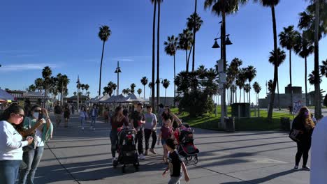 Busy-sidewalk-with-People-wearing-masks,-walking-around-and-riding-bikes-at-the-entrance-to-the-Venice-Beach-Boardwalk-in-Los-Angeles,-California,-USA-during-Covid-19-Pandemic