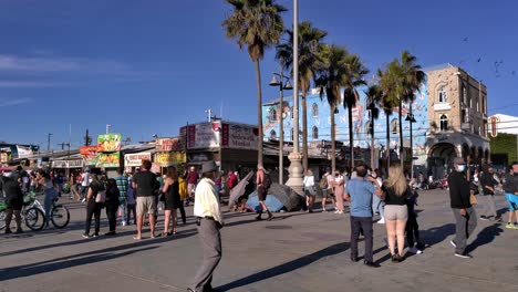 People-wearing-masks-and-walking-around-looking-at-shops-and-birds-flying-around-at-the-Venice-Beach-Boardwalk-during-covid-19-in-Los-Angeles,-California,-USA