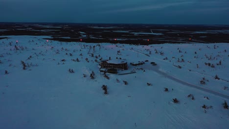 Aerial-view-of-the-Tuikku-restaurant,-blue-hour-in-Levi,-Lapland---pull-back,-drone-shot