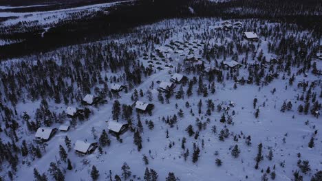 Aerial-view-over-cottages,-towards-aurora-igloos,-in-Lapland---tilt,-drone-shot