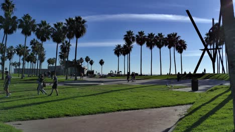 People-leaving-a-grassy-park-at-Venice-Beach-Boardwalk-in-Los-Angeles,-California,-USA---Handheld-static-shot