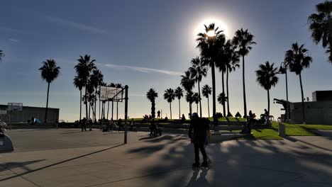 People-walking-around-and-roller-skating-on-Basketball-Court-at-the-Venice-Beach-Boardwalk-in-the-later-afternoon-in-Los-Angeles,-Califonia,-USA