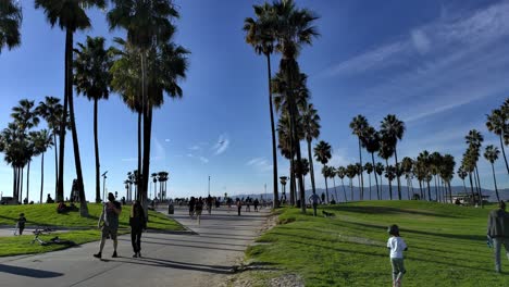 A-crowd-of-people-walking-along-pathways-at-the-Venice-Beach-Boardwalk-on-a-sunny-winter-day-in-Los-Angeles,-California,-USA---Handheld-static-shot
