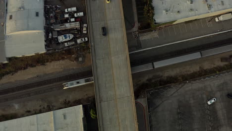 Aerial-drone-view-of-train-passing-by-beneath-freeway-overpass