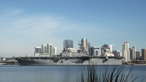 Large-Naval-battleship-passing-by-Downtown-San-Diego-skyline,-background-cityscape