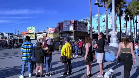 People-wearing-masks-and-gathering-to-watch-a-performance-at-the-Venice-Beach-Boardwalk-during-covid-19-in-Los-Angeles,-California,-USA