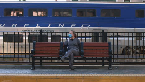 Nurse-in-uniform-wearing-protective-face-mask-sitting-on-bench-waiting-for-train