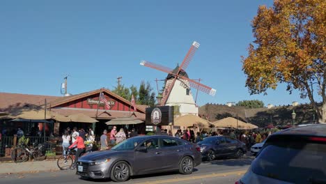 Cars,-an-old-windmill,-and-people-at-a-restaurant,-in-the-Solvang-village,-California,-USA,-sunny-day---Handheld-Static