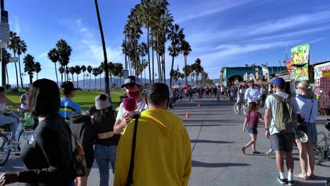 People-wearing-masks,-walking-around-and-gathering-to-watch-a-performance-at-the-Venice-Beach-Boardwalk-during-covid-19-in-Los-Angeles,-California,-USA