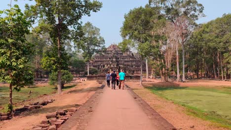 Walking-towards-Ba-Phuon-temple-following-a-road-sided-by-trees-in-a-hot-day