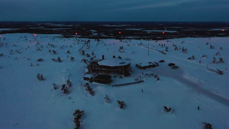 Aerial-view-of-the-Tuikku-restaurant,-blue-hour-in-Levi,-Lapland---reverse,-drone-shot
