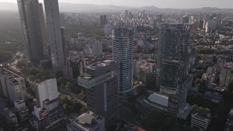 Wolkenkratzer-In-Der-Innenstadt-Von-Mexiko-Stadt-Und-Nebliges-Stadtbild-Am-Sonnigen-Abend,-Drohnenaufnahme,-Luftaufnahme