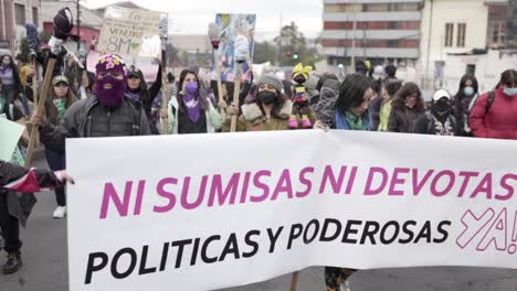 Women-are-holding-up-a-big-sign-and-flag-with-a-phrase-in-protest-while-marching-during-the-International-Women's-day-in-Quito,-Ecuador