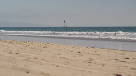 Pacific-Ocean-Waves-on-Santa-Monica-Beach,-Sailing-Boat-and-Surfer-on-Sunny-Day