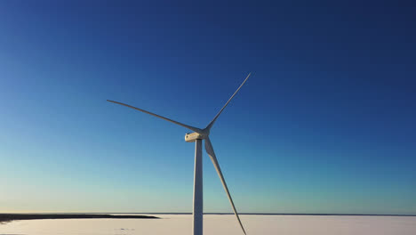 Aerial-view-around-a-wind-turbine,-sunny,-winter-day,-at-frozen-sea---orbit,-drone-shot