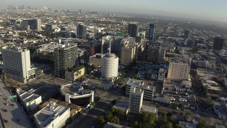 Aerial-View-of-Capitol-Records-Building,-Hollywood-and-Downtown-Los-Angeles-CA-USA-in-Background,-Revealing-Drone-Shot