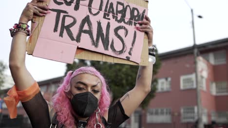 Eine-Transfrau-Mit-Rosa-Haaren-Und-Maske-Hält-Ein-Schild-Hoch,-Um-Gegen-Die-Gewalt-Gegen-Transsexuelle-Und-Transvestiten-Während-Des-Internationalen-Frauentags-In-Quito,-Ecuador,-Zu-Protestieren