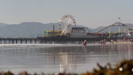 Santa-Monica-Pier-and-Beach,-People-Walking-on-Sand-on-Sunny-Evening-Slow-Motion