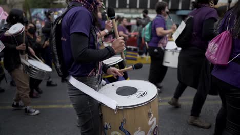 Several-women-dresses-in-purple-are-playing-drums-while-marching-during-the-protest-in-the-International-Women's-day-in-Quito,-Ecuador
