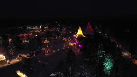 Aerial-Night-Side-View-of-Vibrant-Colours-of-Santa-Claus-Village,-Finland,-Orbit-Shot