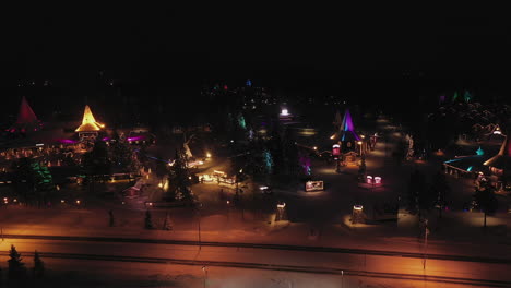 Aerial-Wide-View-of-Bright-Lights-of-Santa-Claus-Village-from-Roadside,-Finland,-Established-Shot