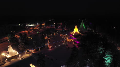 Nighttime-Aerial-of-Glowing-Sparkling-Red,-Gold-and-White-Rooftops-of-Santa-Claus-Village,-Finland,-Zoom-out