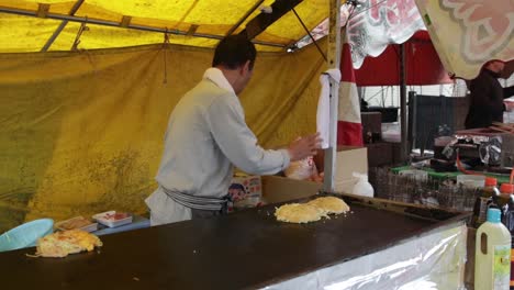 Japanese-street-food-chef-cooking-tasty-Okonomiyaki-in-Kyoto,-Shinto-Shrine