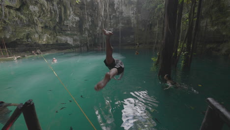 Back-of-a-Man-Jumping-From-Platform-Into-Turquoise-Water-of-Mexican-Cenote,-Slow-Motion-Full-Frame
