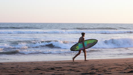 Surfer-With-Surfboard-Walking-on-Sandy-Beach-by-Ocean-Waves,-Slow-Motion