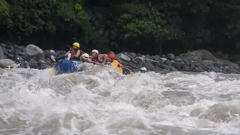 A-group-of-tourists-rafting-in-Baños,-Ecuador,-are-rowing-and-slowly-passing-through-a-strong-current-and-waves-of-a-river