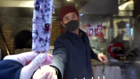 Person-selling-street-food-handing-to-the-camera-and-a-hand-grabbing-sticky-rice-and-red-beans-on-a-stick