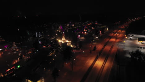 Nächtliche-Luftaufnahme-Einer-Ruhig-Beleuchteten-Straße-Neben-Leuchtenden-Lichtern-Des-Weihnachtsmanndorfes,-Finnland,-Schwenkaufnahme