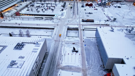 Aerial-view-following-a-yellow-taxi-on-the-snowy-streets-of-Oulu,-dawn-in-Finland