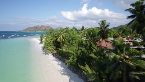 Drone-Volando-Sobre-La-Playa-De-Cote-D&#39;or-Cerca-De-Palmeras-Y-Restaurantes,-Seychelles