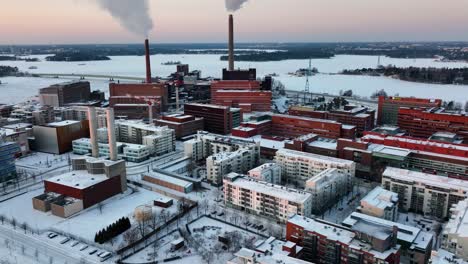 Aerial-view-of-smoking-chimneys,-winter-sunset-in-Helsinki,-Finland---tracking,-drone-shot