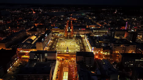Flying-toward-the-night-lit-market-square,-winter-in-Vaasa,-Finland---Aerial-view