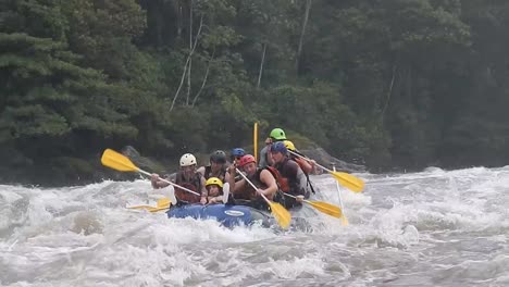 Tourists-rafting-in-Baños,-Ecuador,-they-are-rowing-with-their-oars-on-a-strong-river-with-waves