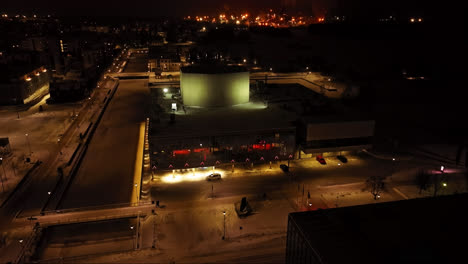 Drone-shot-away-from-the-night-lit-Oulu-Theatre,-winter-evening-in-Finland