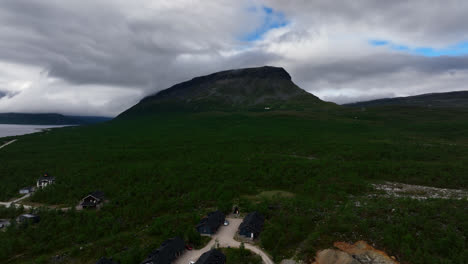 Aerial-view-ascending-in-front-of-a-resort-with-the-Saana-fell-in-the-background,-cloudy,-summer-day-in-Kilpisjarvi,-Finland