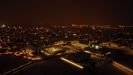 Aerial-view-backwards-away-from-the-market-and-the-skyline,-winter-night-in-Oulu