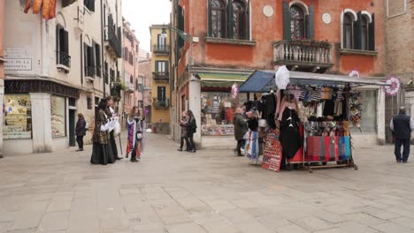 Street-view-in-Venice-after-the-cancelled-Carnival,-Couple-in-venetian-costumes-near-a-street-vendor