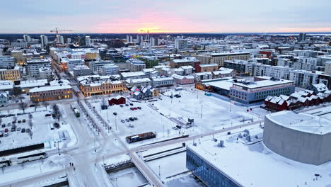 Aerial-circling-shot-overlooking-the-snowy-market-square-of-Oulu-city,-winter-evening-in-Finland